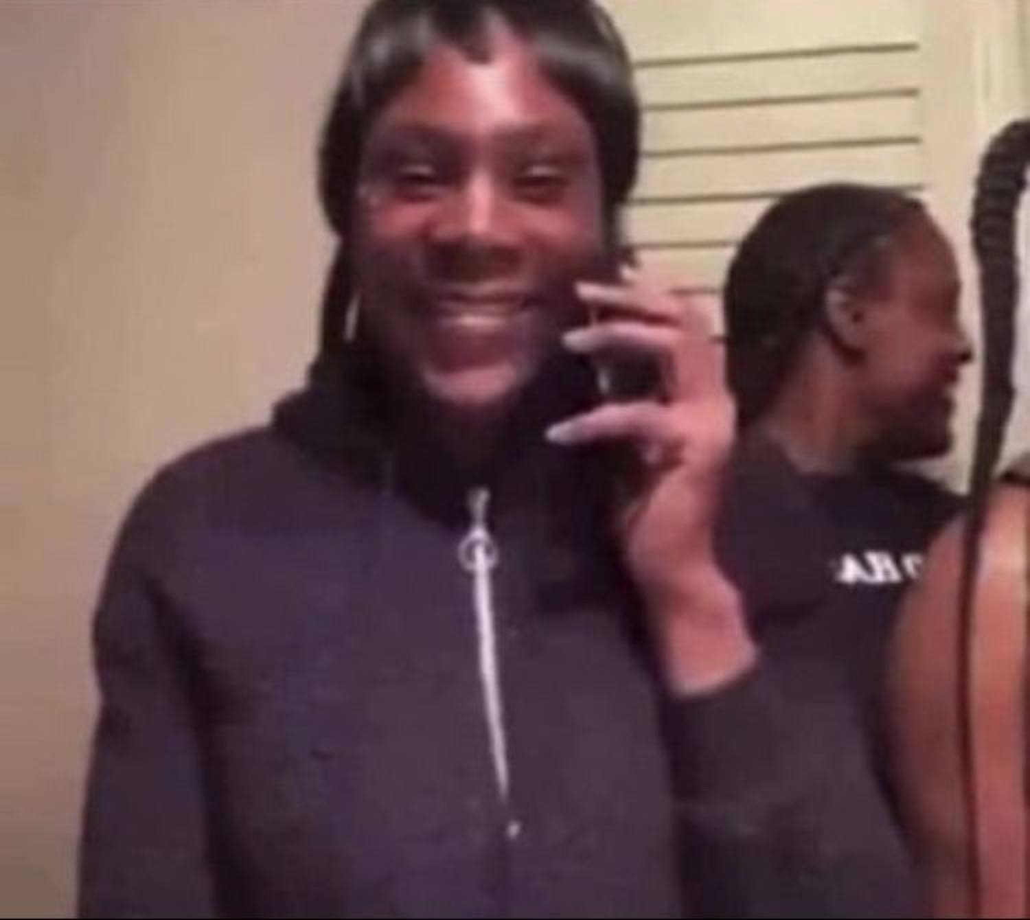 Person with a wig on the phone flashing a big grin while someone lingers behind them