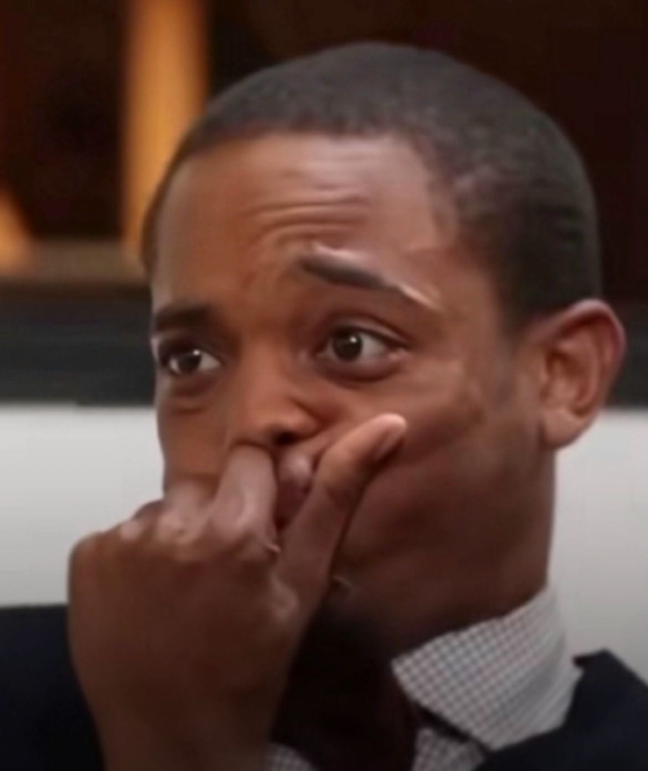 Man covering his mouth with his fist, eyes wide in nervous, awkward tension