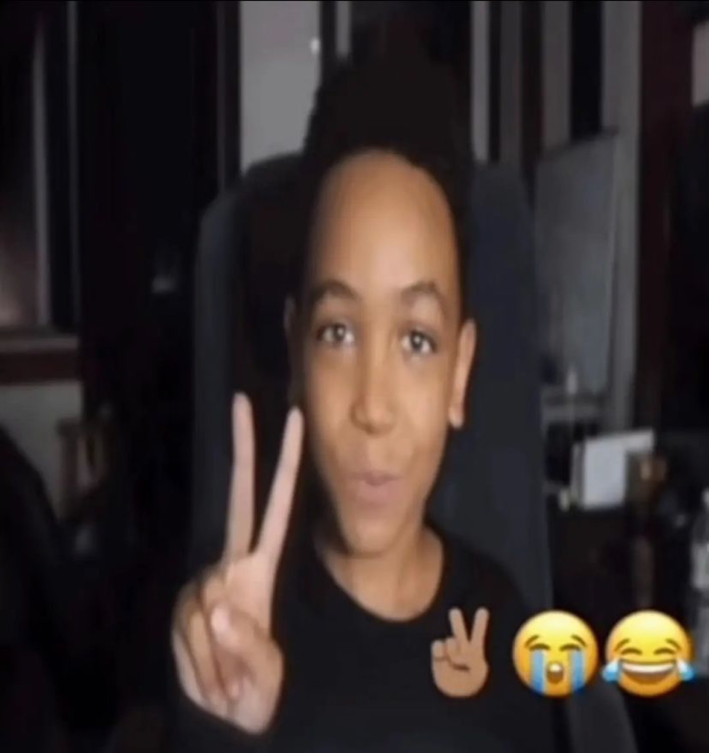 Young guy throwing up a peace sign with crying-laugh emojis on screen beside him