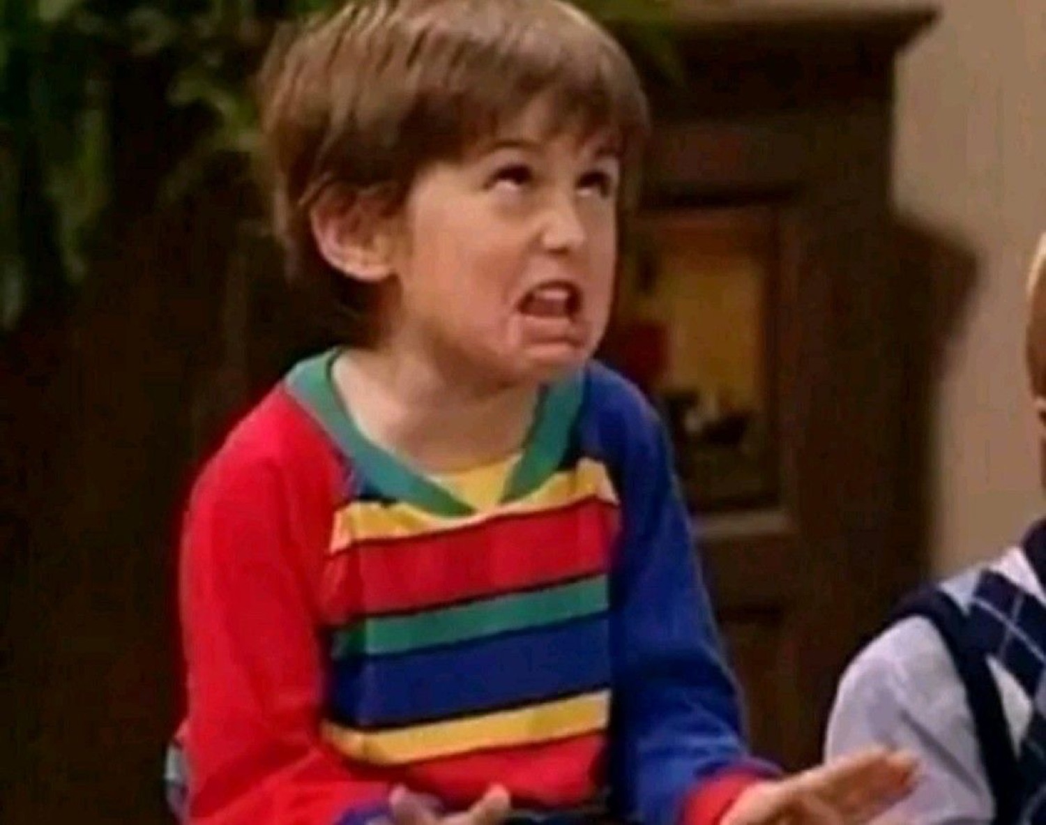 Kid in a rainbow-striped shirt baring his teeth in a disgusted, cringing grimace