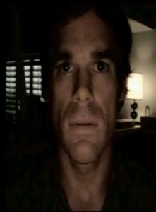 Man's face half-lit in a dark room with an empty, exhausted blank stare