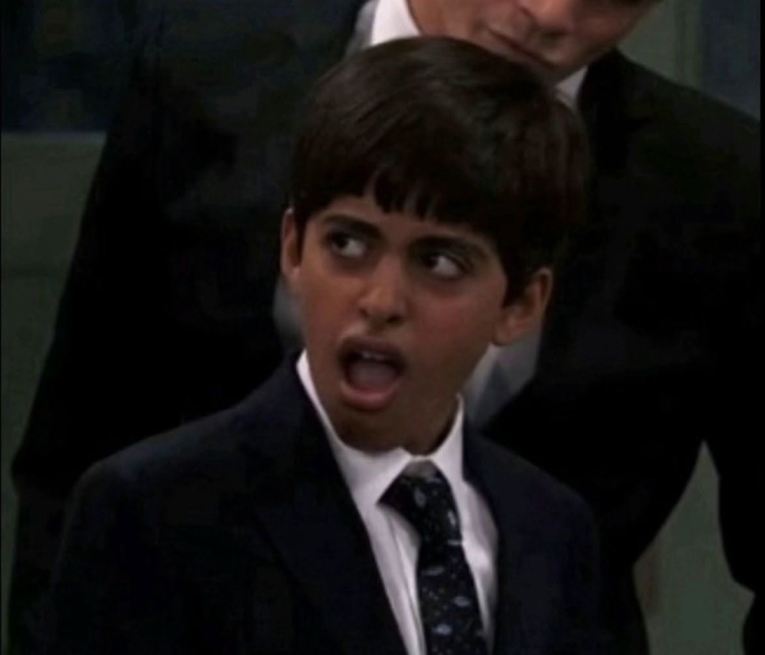 Young boy in a suit with mouth wide open and eyes darting sideways in total shock