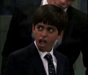 Young boy in a suit with mouth wide open and eyes darting sideways in total shock