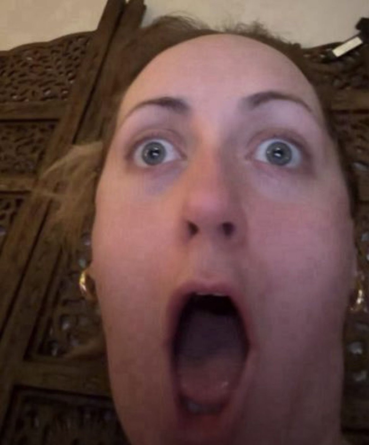 Woman's face filling the frame with enormous wide eyes and a jaw-dropped open mouth in total shock