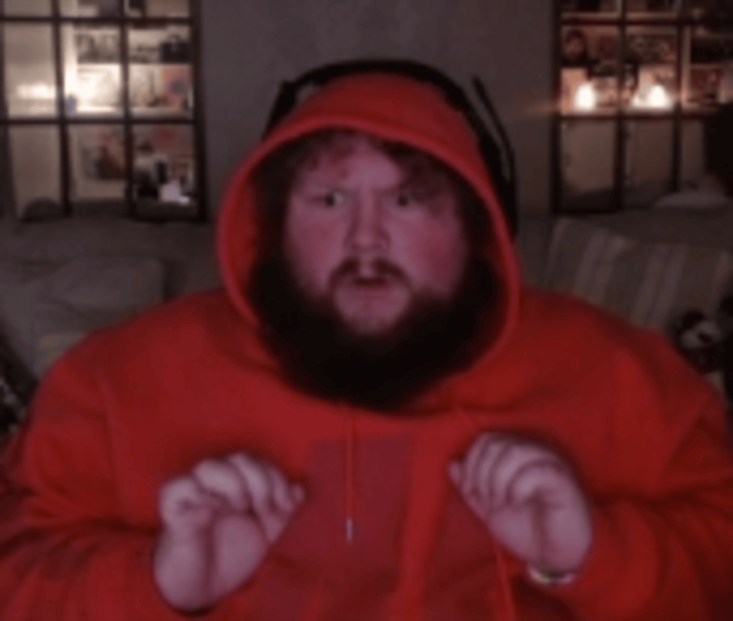 Bearded streamer buried in a huge red hoodie, wide-eyed and clenching both fists