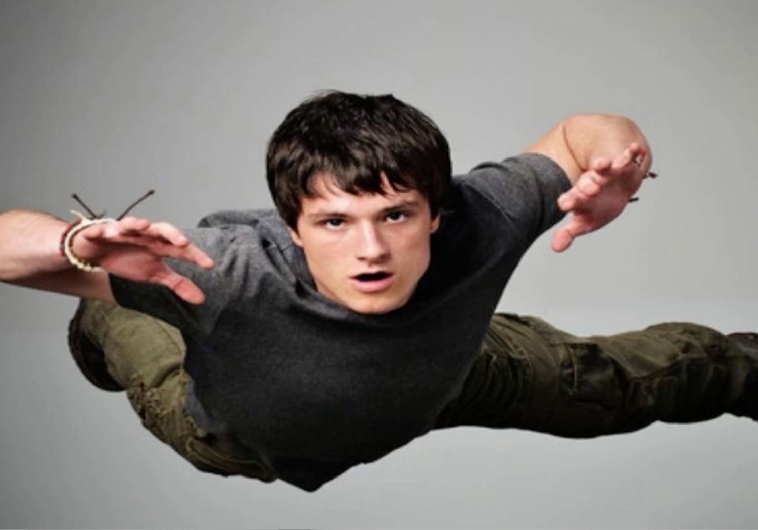 Young man in a grey sweater posing mid-air as if flying with arms spread