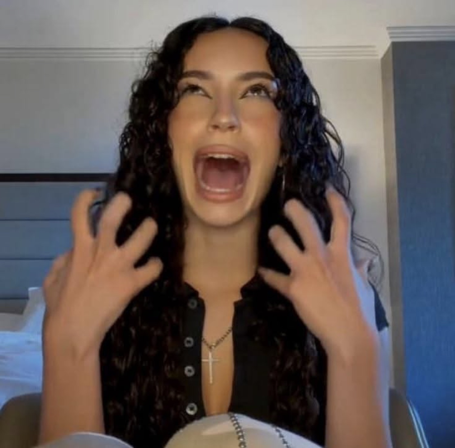 Dark-haired woman in a black top screaming with both hands raised in alarm