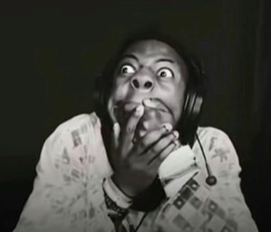 Streamer wearing headphones staring in wide-eyed terror at the screen, hands clasped near their face