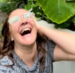 Woman in glasses throwing her head back cackling with a hand on her head