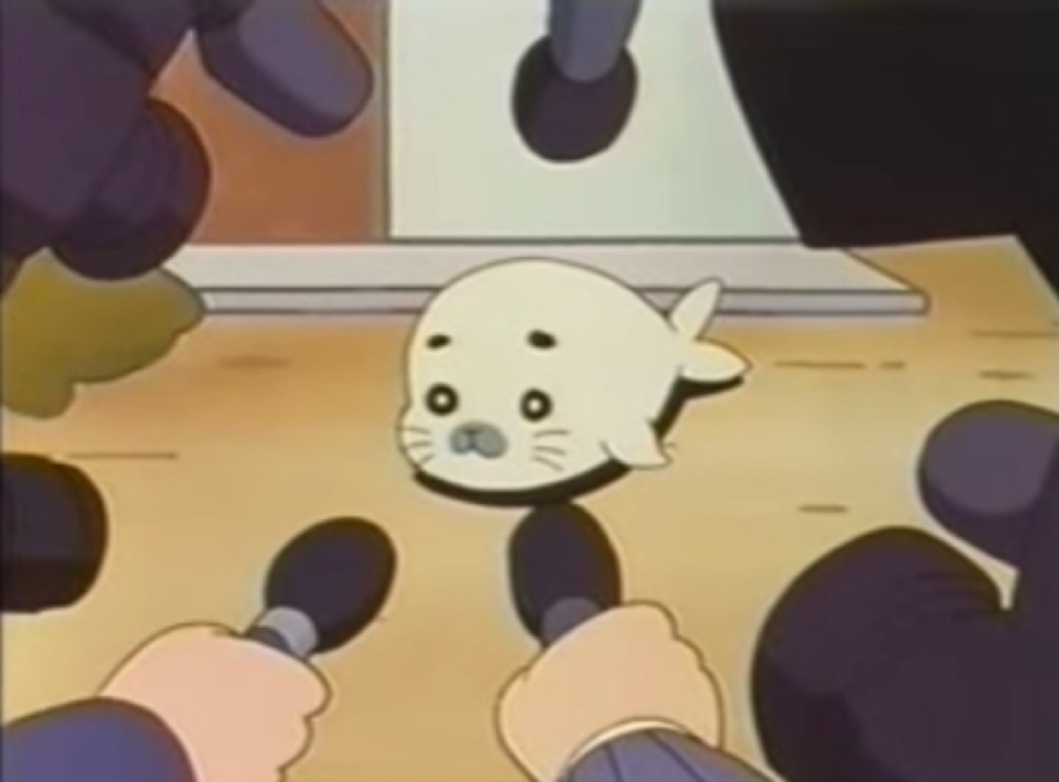 Tiny wide-eyed cartoon baby seal cornered by a ring of pointing microphones