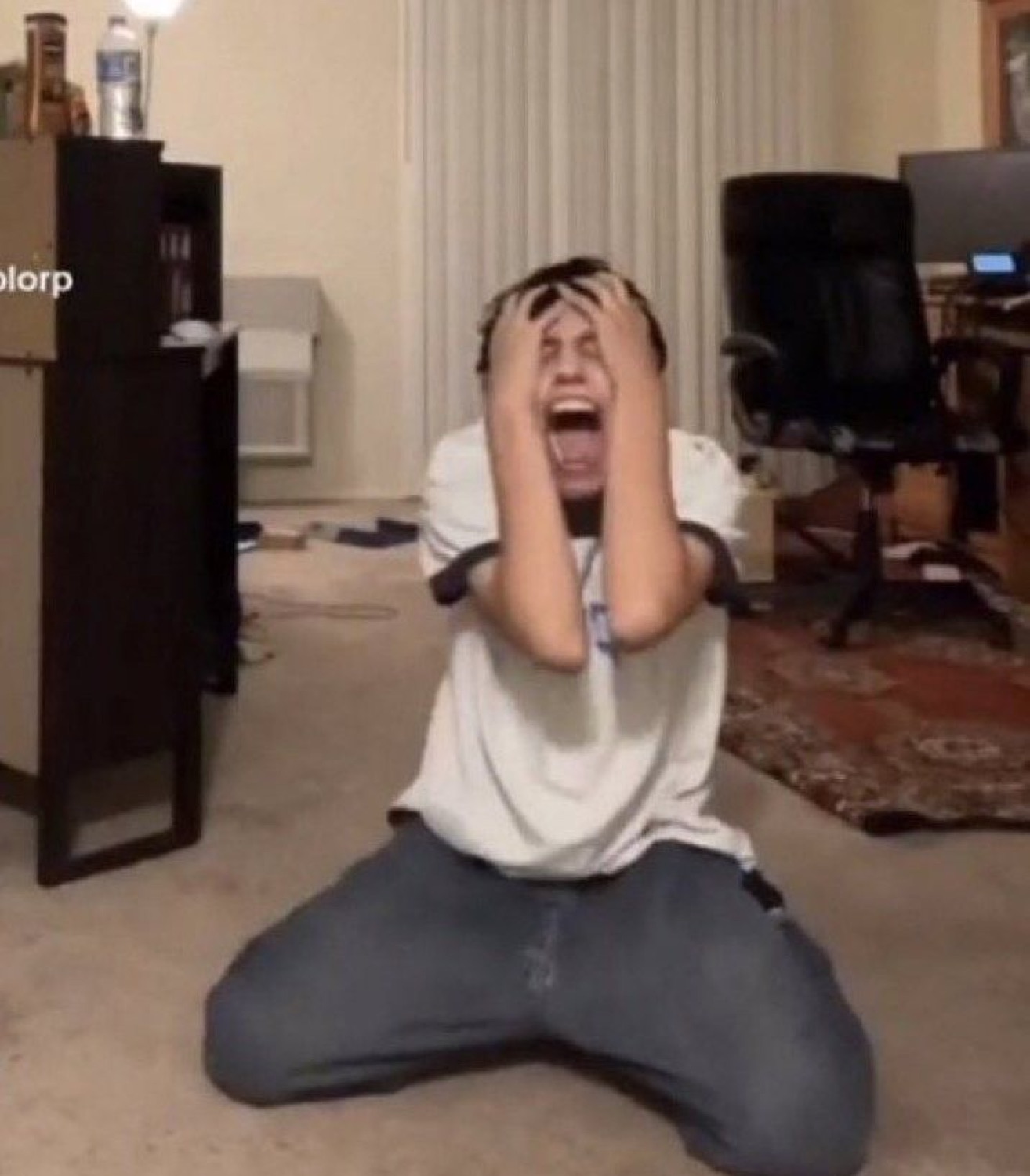Guy on his knees clutching his head and screaming in an empty living room