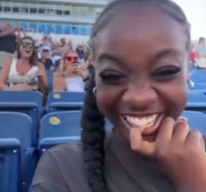 Woman in stadium seats cracking up with a huge grin, biting her finger from laughing