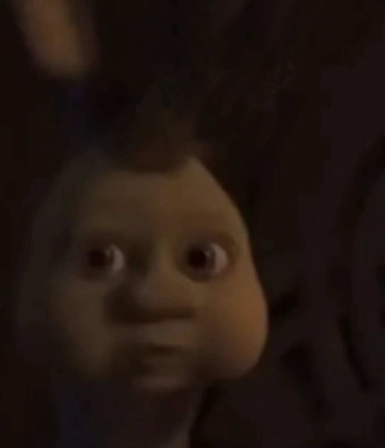 Dimly lit CGI doll face with wide eyes staring out of the shadows