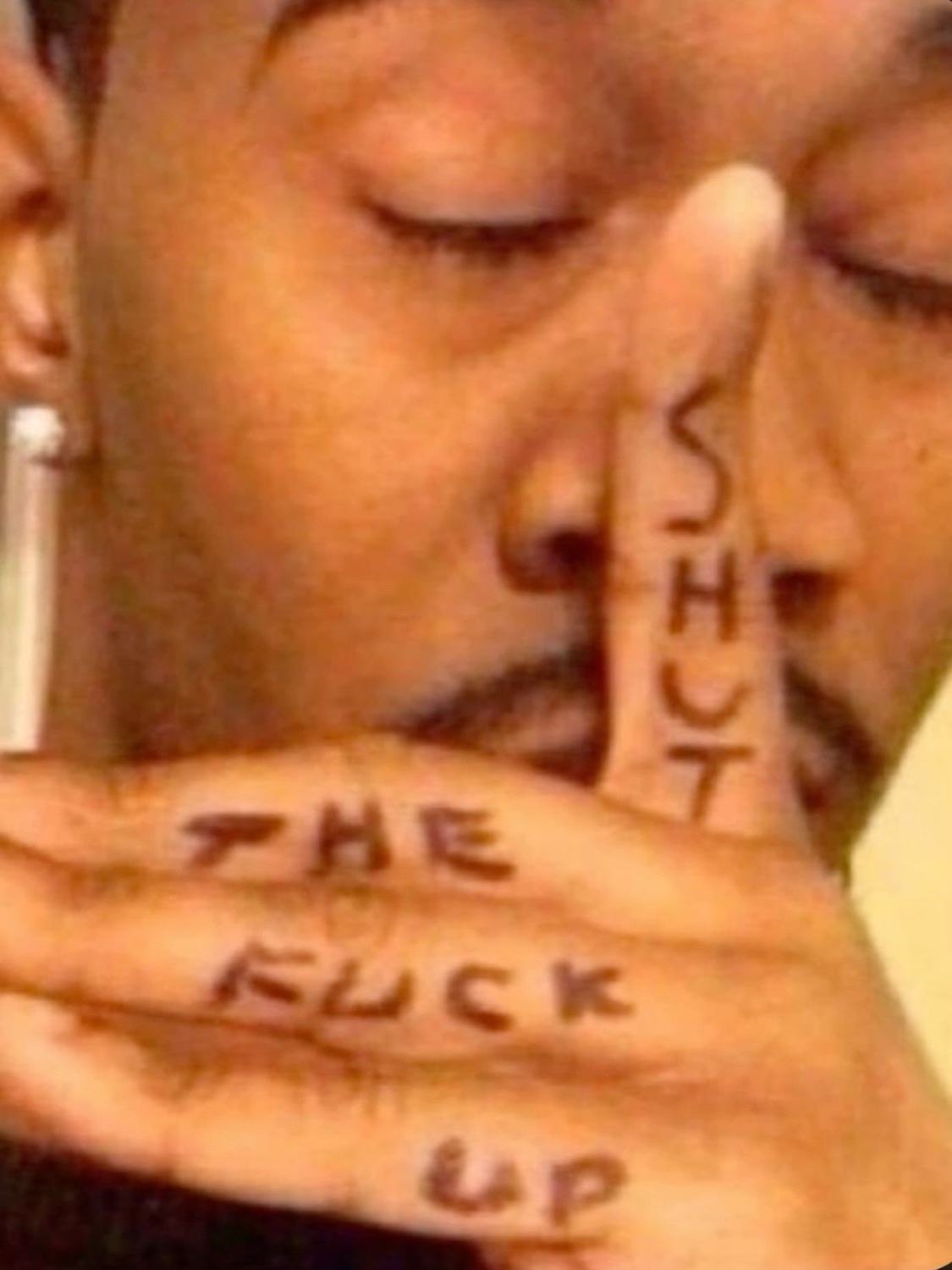 Person with 'SHUT THE FUCK UP' written across their fingers and hand held up to their face