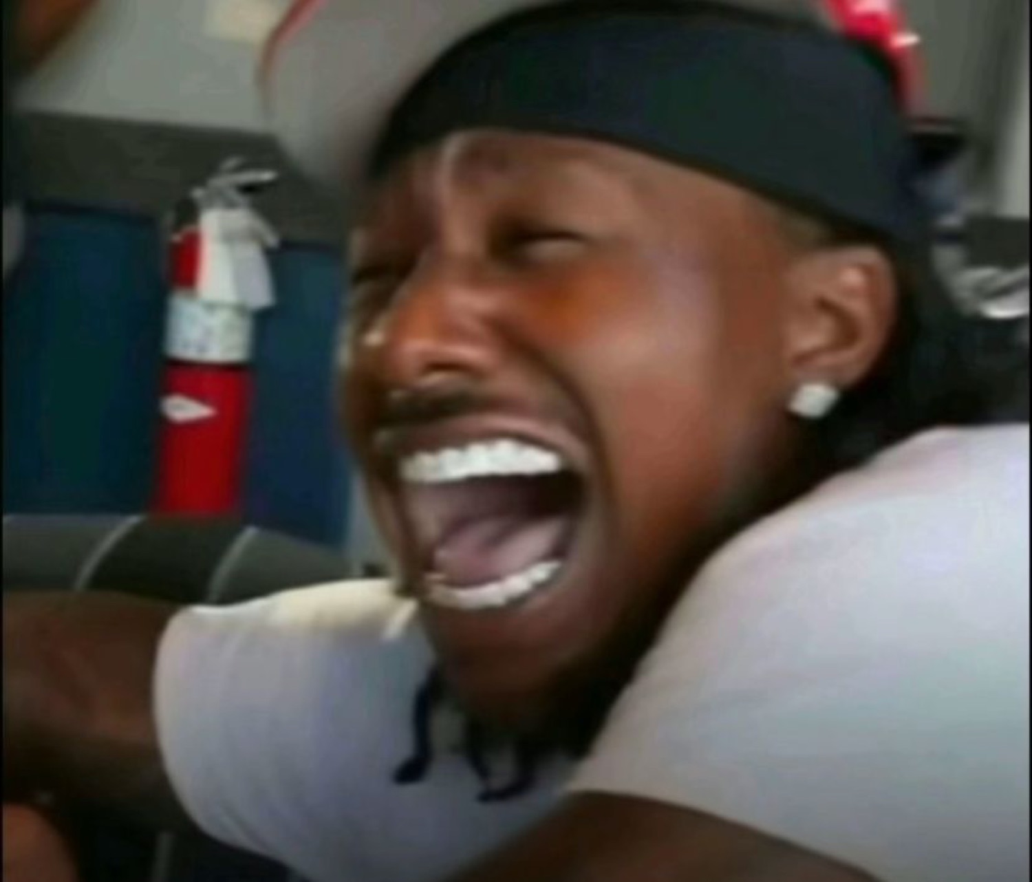 Man on what looks like a bus throwing his head back and cackling with his mouth wide open
