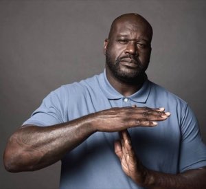Shaquille O'Neal in a blue polo giving a firm timeout hand gesture with a deadpan stare