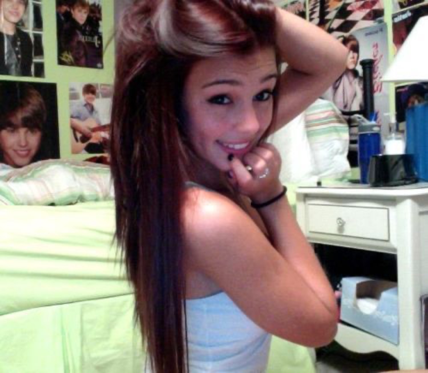 Young woman looking back over her shoulder with a flirty smile, Justin Bieber posters covering the bedroom wall