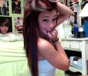 Young woman looking back over her shoulder with a flirty smile, Justin Bieber posters covering the bedroom wall