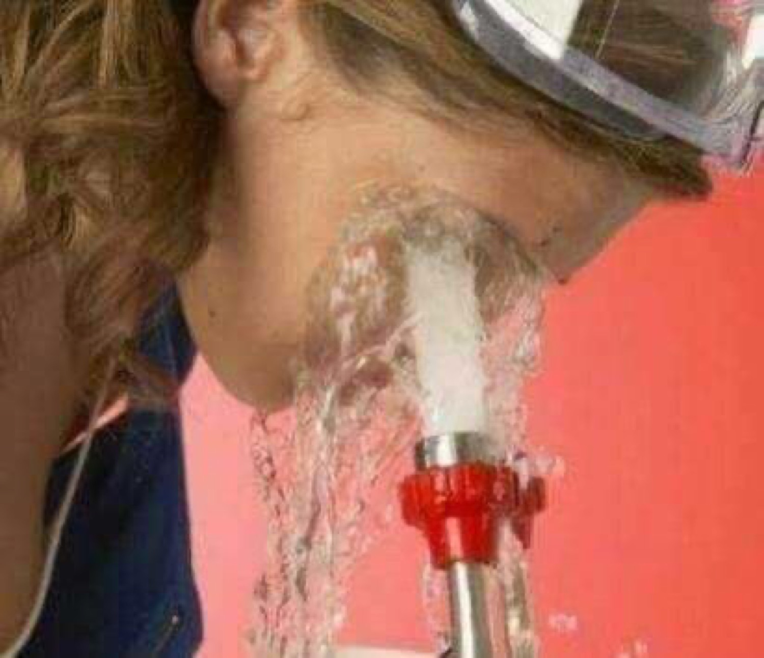 Woman leaning into a fire hose blasting water directly into her face at full pressure