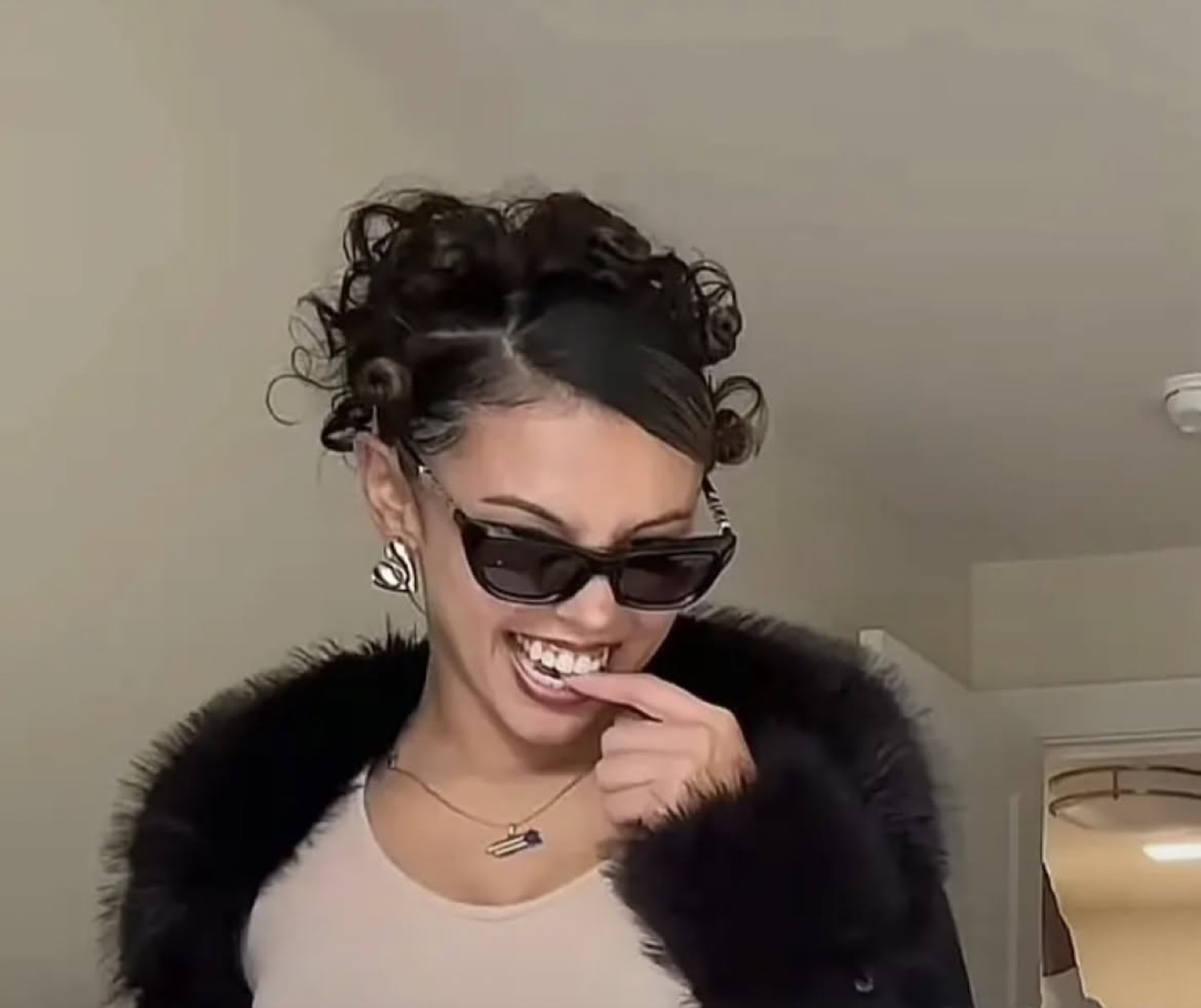 Woman in sunglasses and fur coat biting her finger with a sly, giddy grin