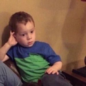 Little kid slouched in a chair with a blank, unbothered stare and a hand at his head