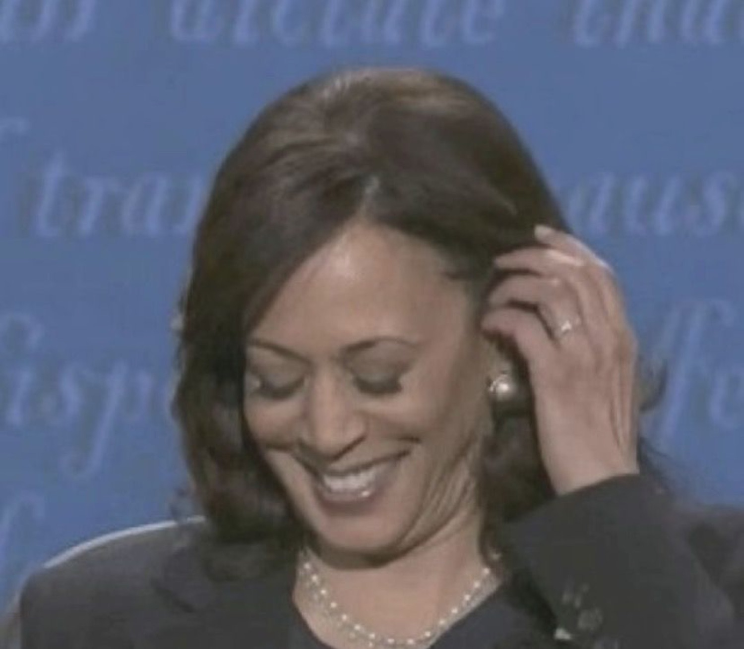 Kamala Harris looking down with a bashful laugh, tucking hair behind her ear