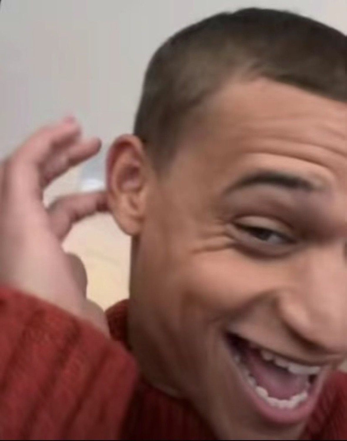 Guy in a red sweater cracking up with a wide, sneaky grin