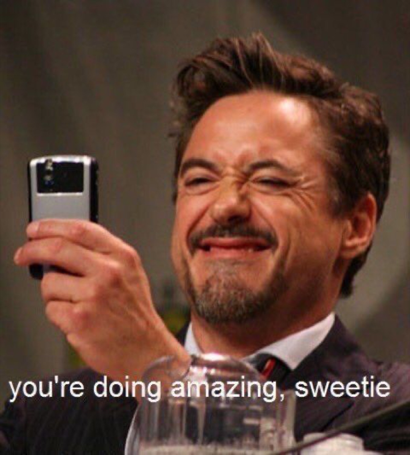 Robert Downey Jr. laughing while holding up a phone, captioned 'you're doing amazing, sweetie'