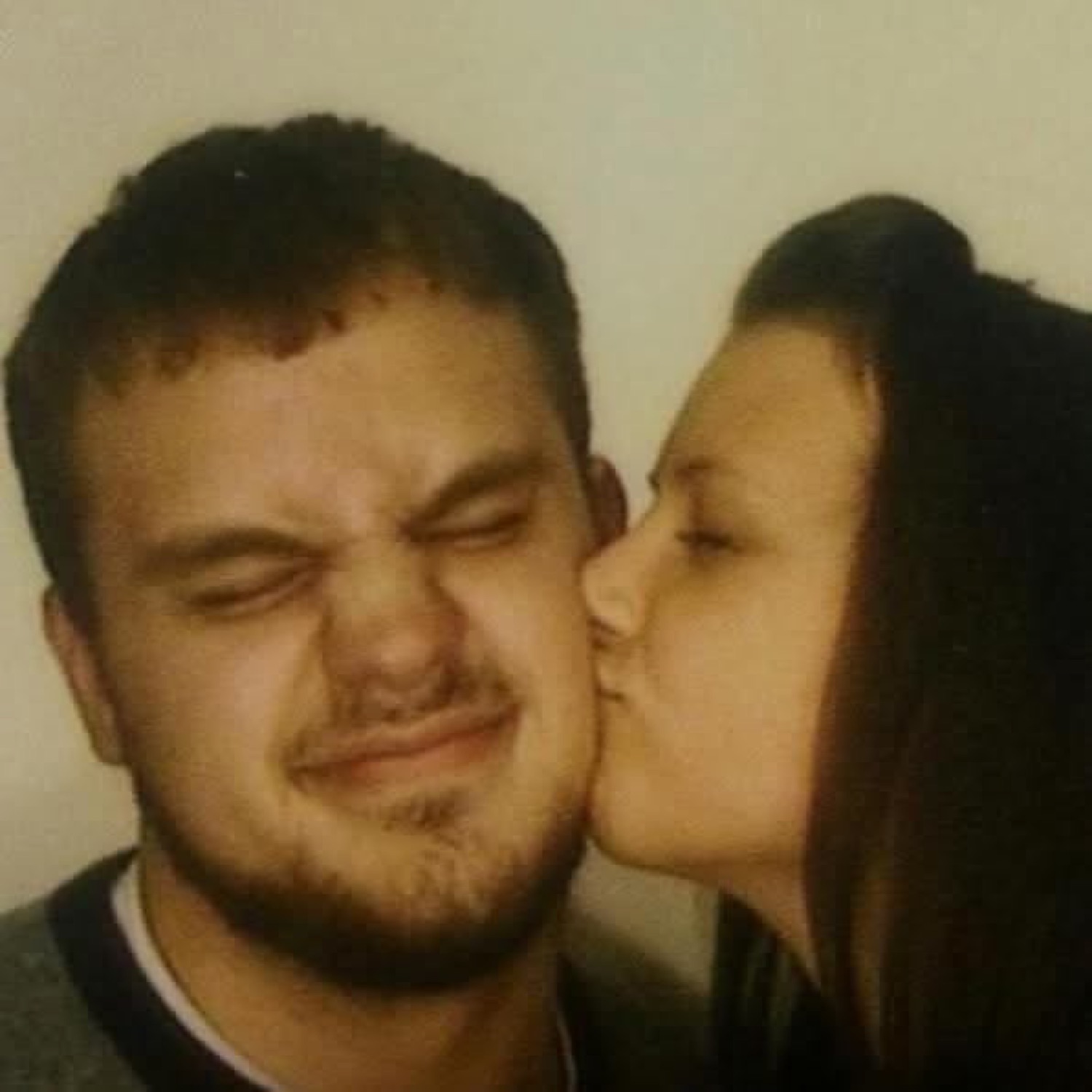 Man scrunching his face while a woman kisses his cheek