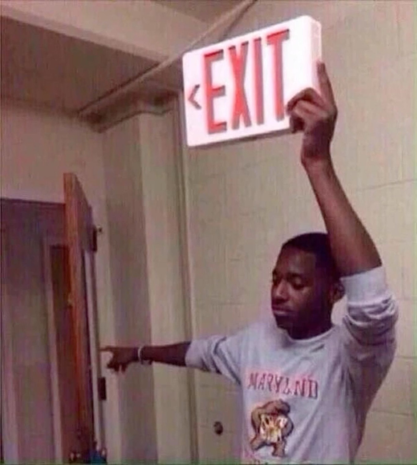 Guy holding up an EXIT sign while deadpan-pointing at the door