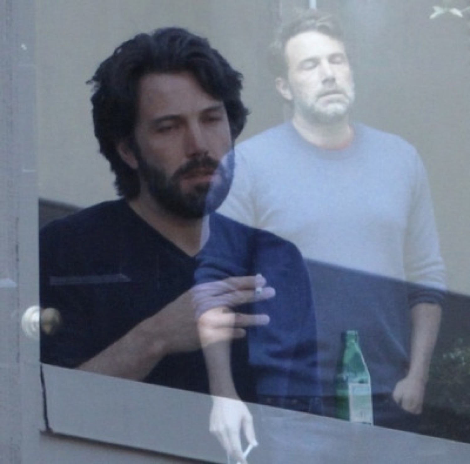 Ben Affleck smoking behind a window looking completely worn out and over it