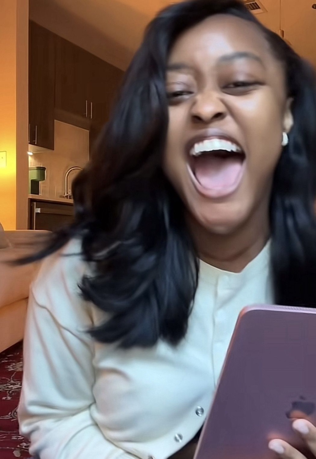 Young woman looking at her phone and screaming with delight, mouth wide open mid-reaction