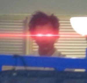 Blurry person with glowing red laser eyes sitting in a dark room
