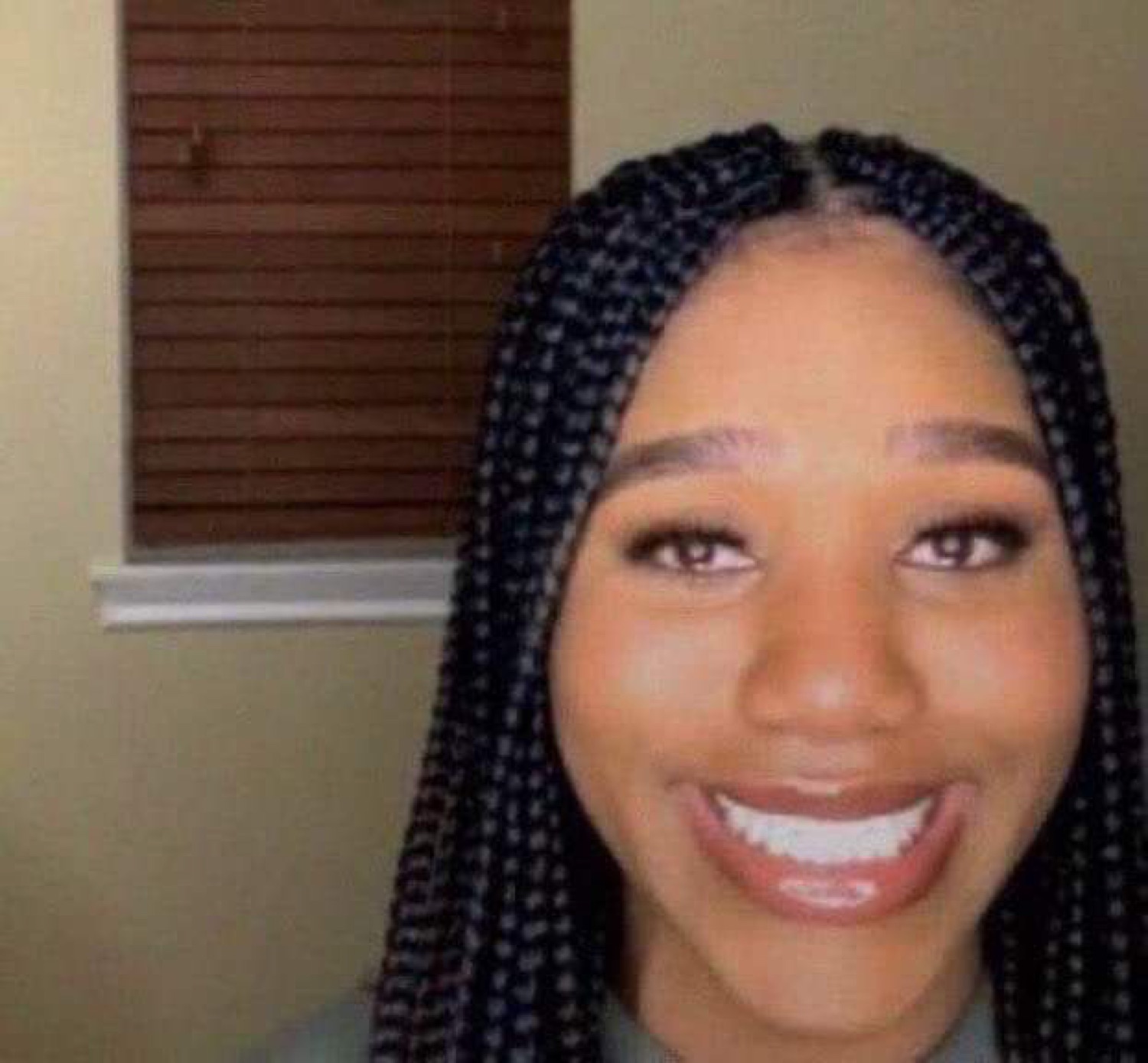 Woman with box braids beaming a wide, delighted grin at the camera