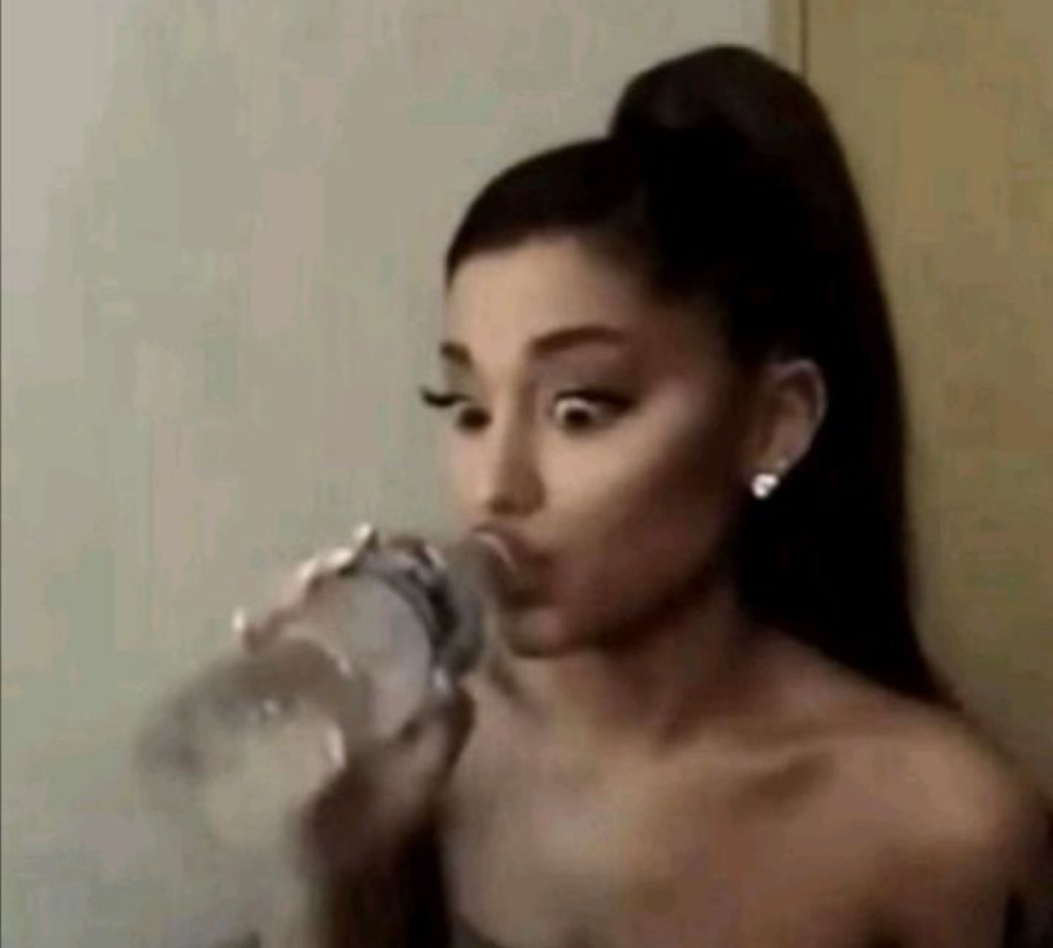 Woman with a high ponytail sipping from a water bottle while side-eyeing off-frame