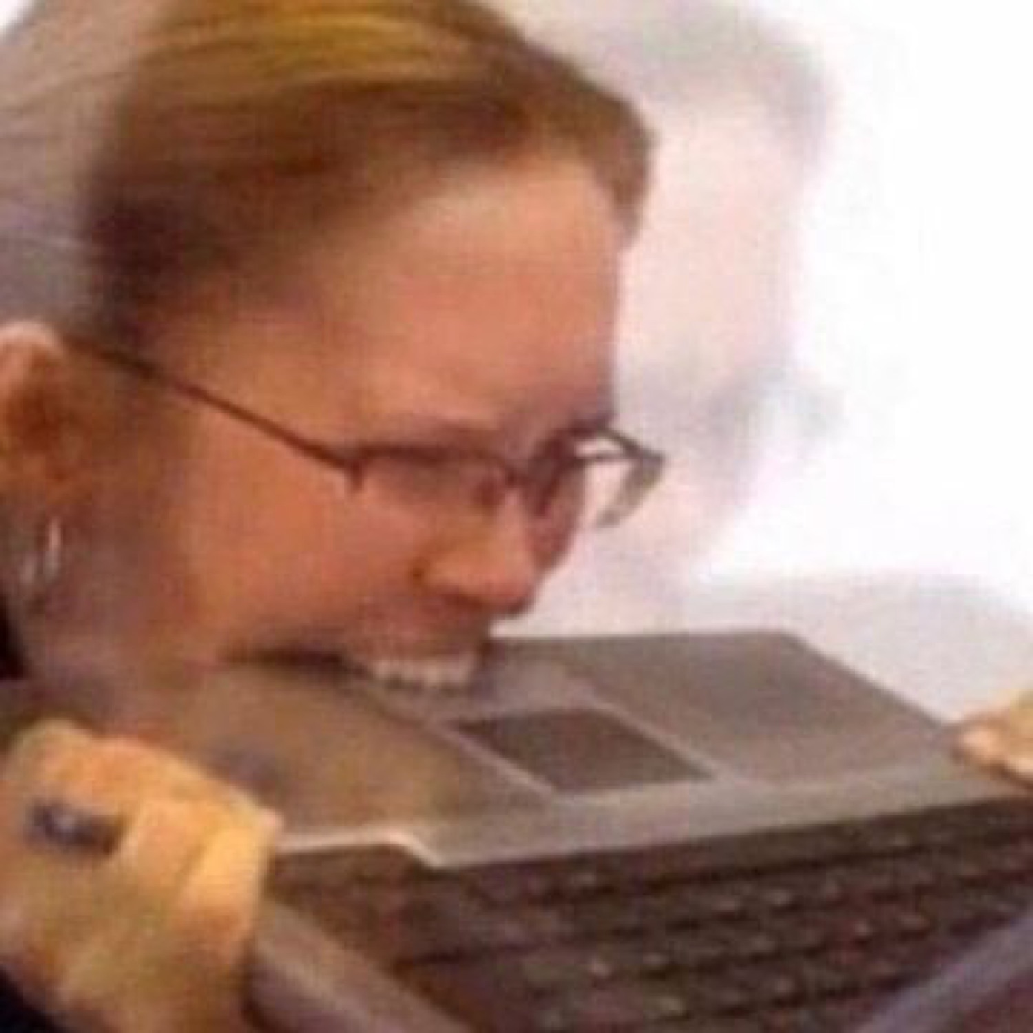 Woman with glasses biting the edge of her laptop in frustration