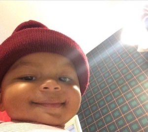 Chubby baby in a red beanie giving the smuggest little smile straight at the camera