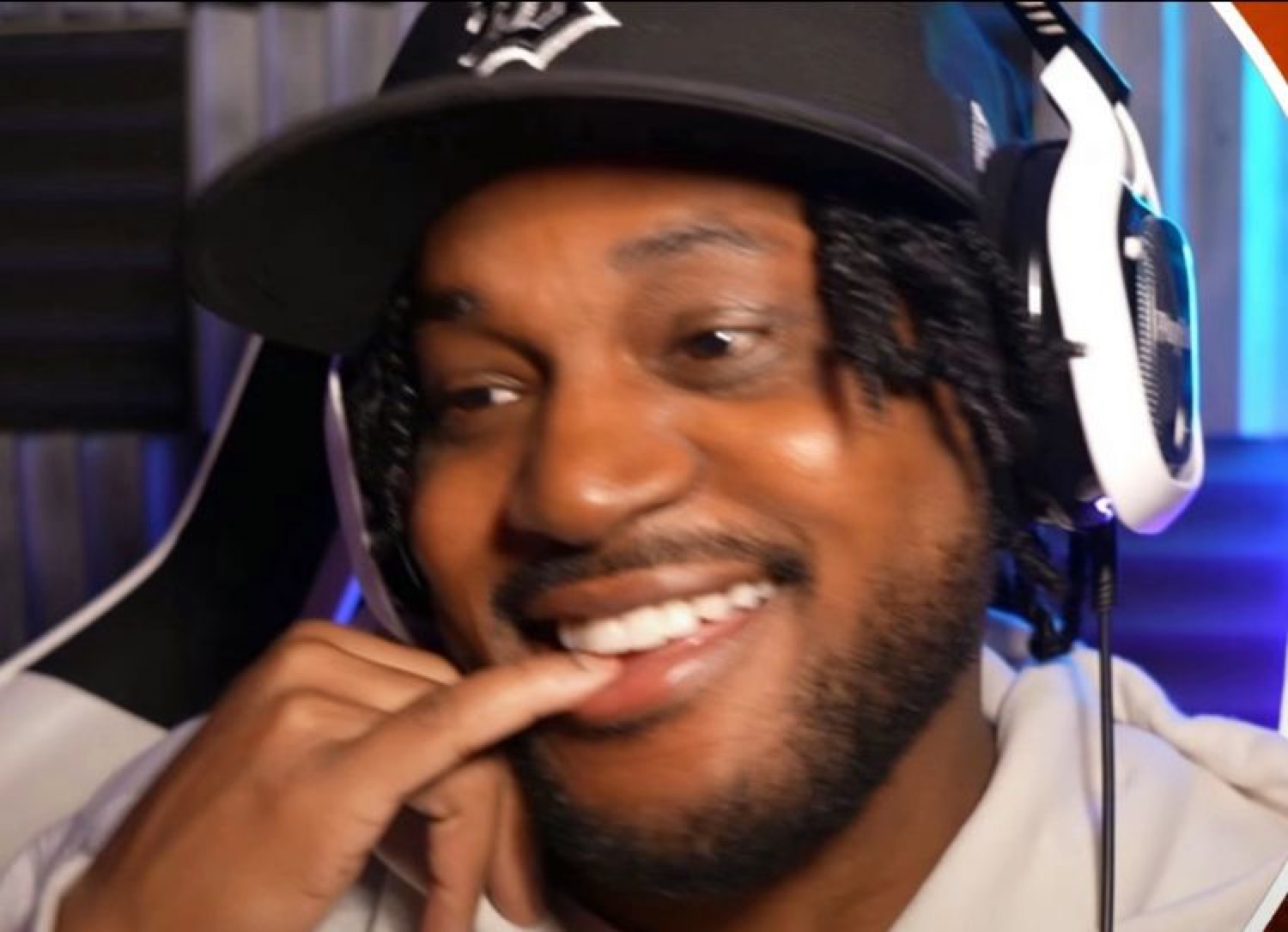 Streamer in a black cap and headset biting his finger with a mischievous grin