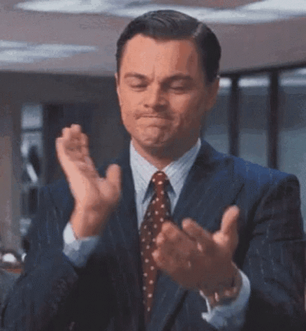 Leonardo DiCaprio in a suit clapping with a satisfied smirk