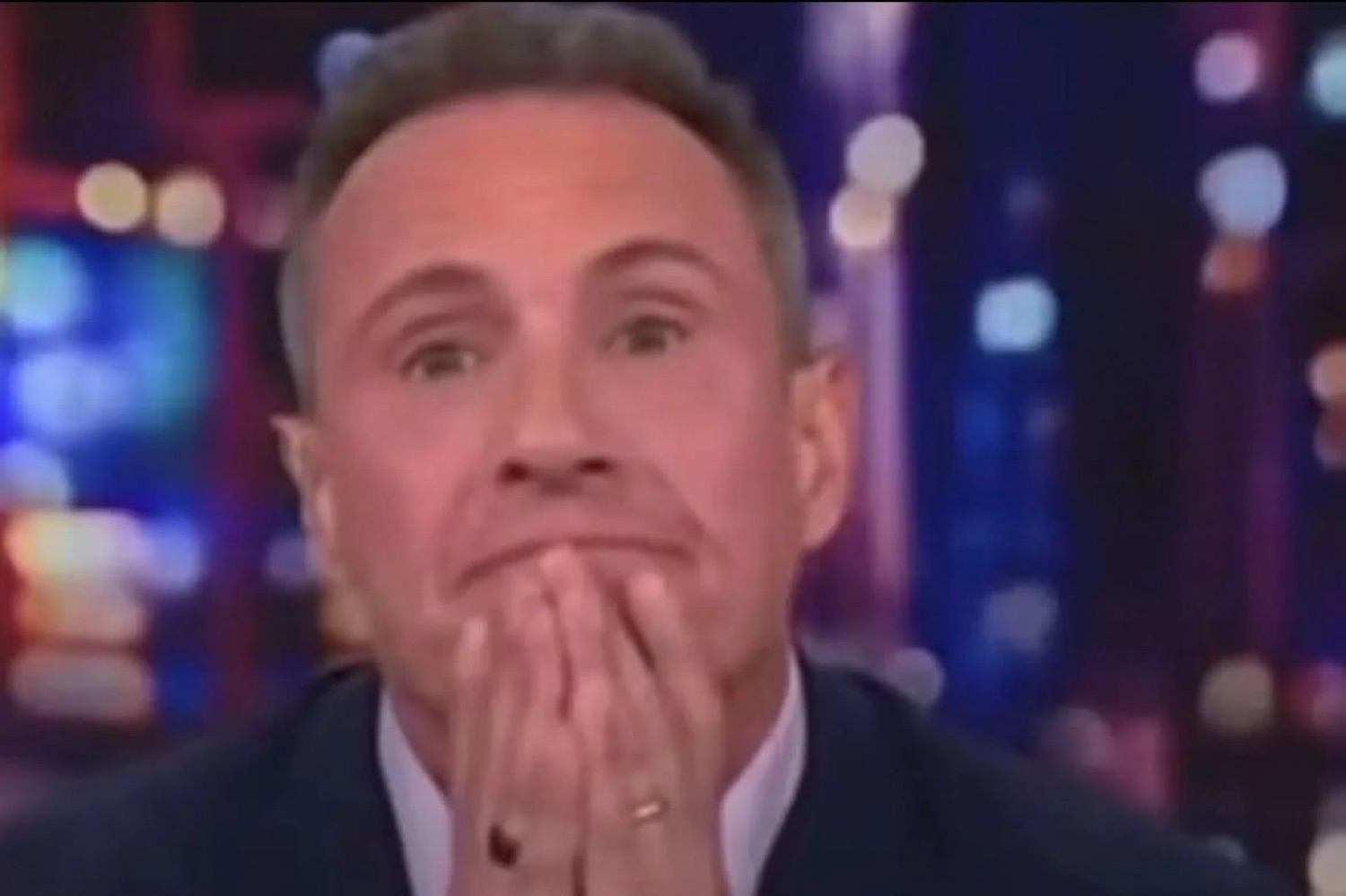 Man at a news desk pressing both hands to his face in visible distress