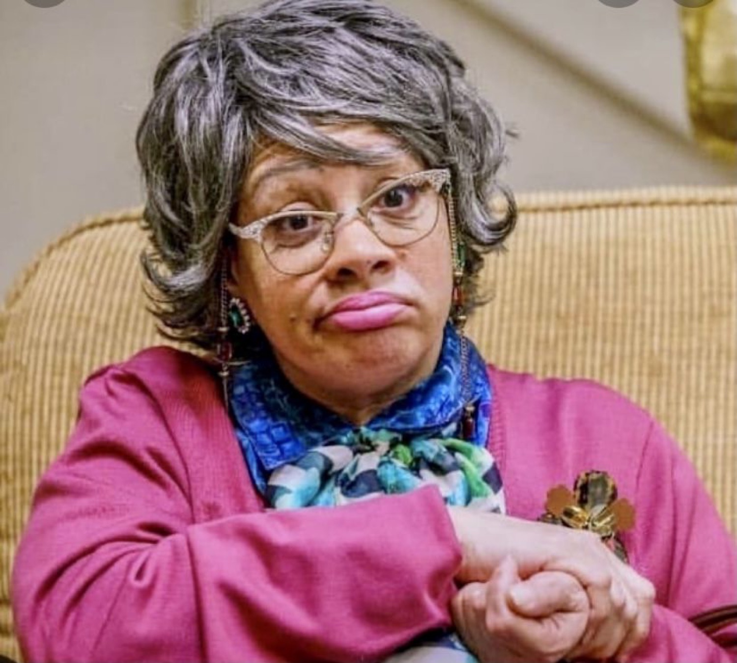 Older woman in a pink cardigan with pursed lips and arms crossed, thoroughly unimpressed