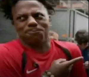 Man in a red shirt side-eyeing and pointing off to the side with a skeptical face