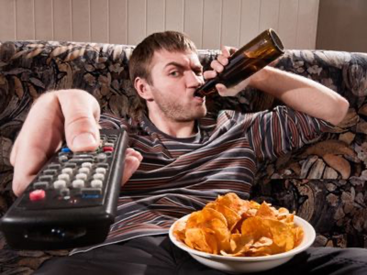 Guy on the couch simultaneously chugging a beer and pointing the remote like it's an emergency