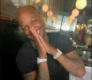Bald tattooed man grinning with hands pressed together, looking extremely pleased with himself