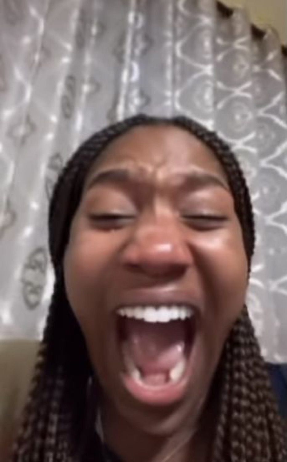 Woman with her eyes shut and mouth wide open mid-scream in front of a curtain
