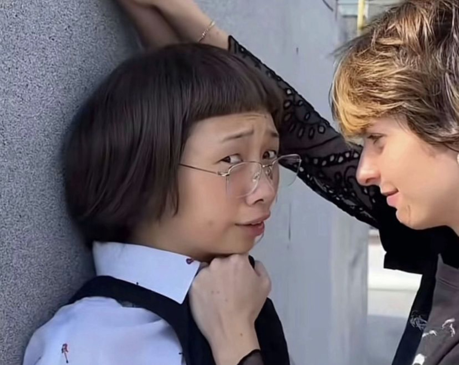 Person pinned against a wall wearing a wide-eyed, cornered look while someone leans in close