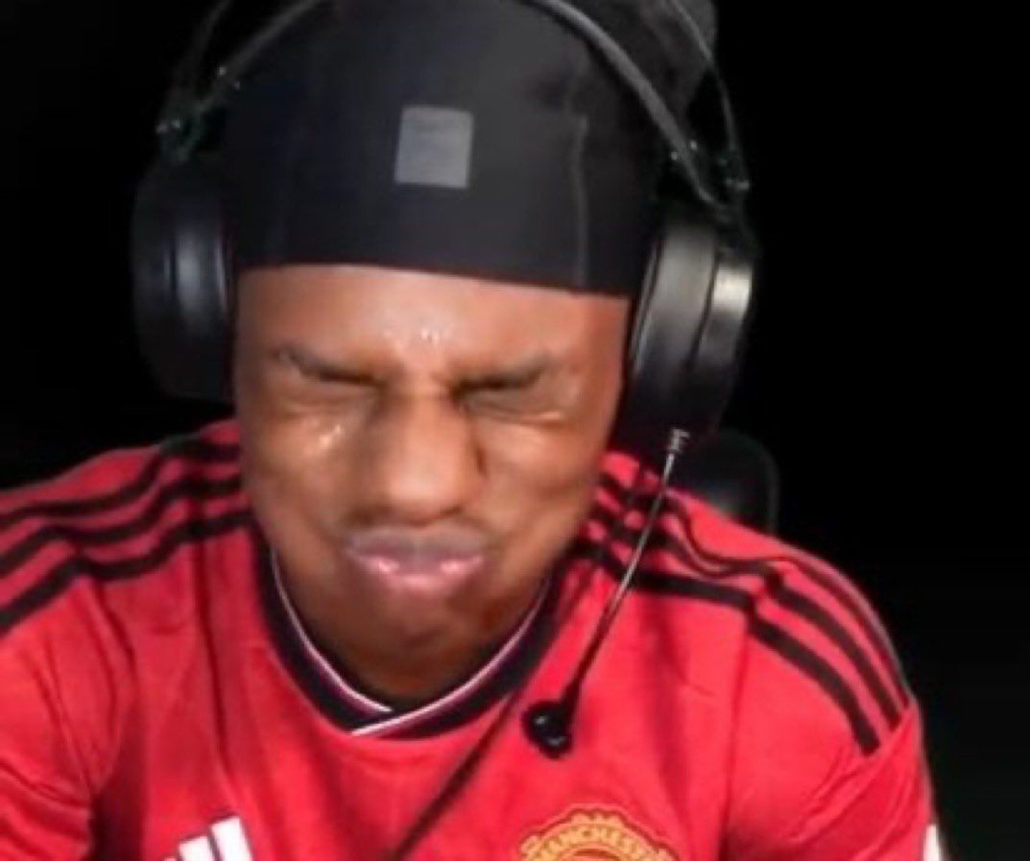 Guy in headphones and a Man United jersey scrunching his face in pained disgust