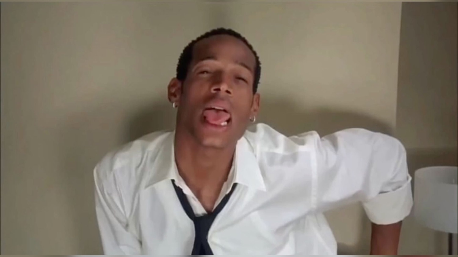 Man in a white shirt and tie leaning back with his tongue out and a wild expression