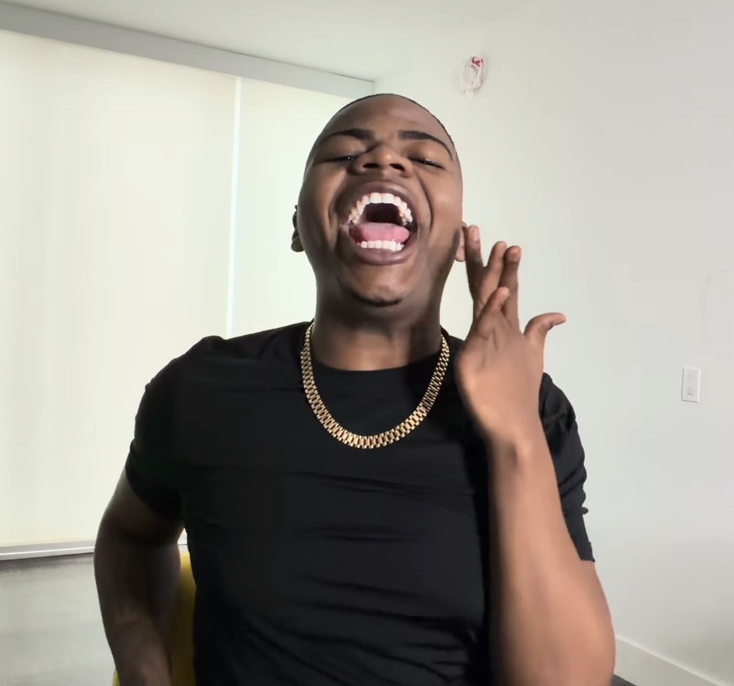 Man in a black tee and gold chain throwing his head back mid-laugh