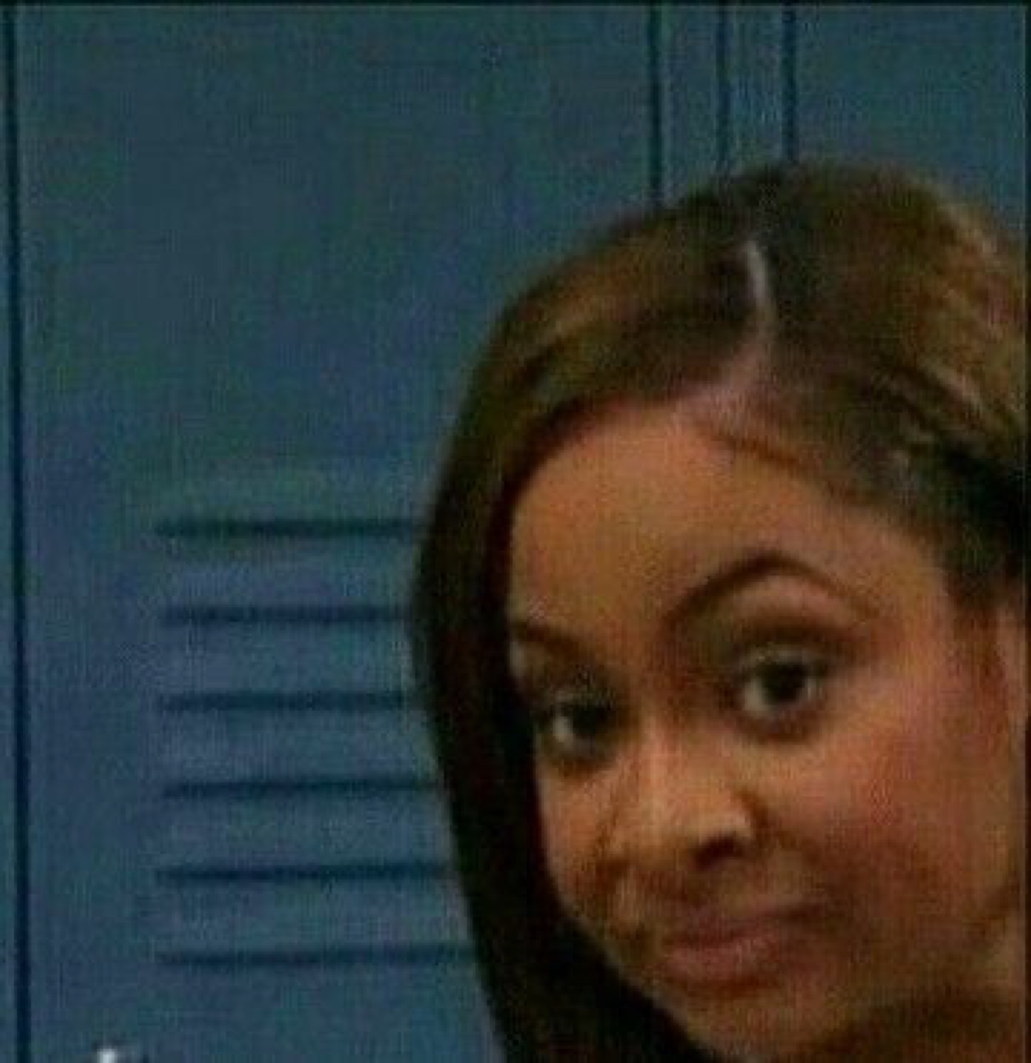 Girl by a locker giving a nervous sideways glance at the camera